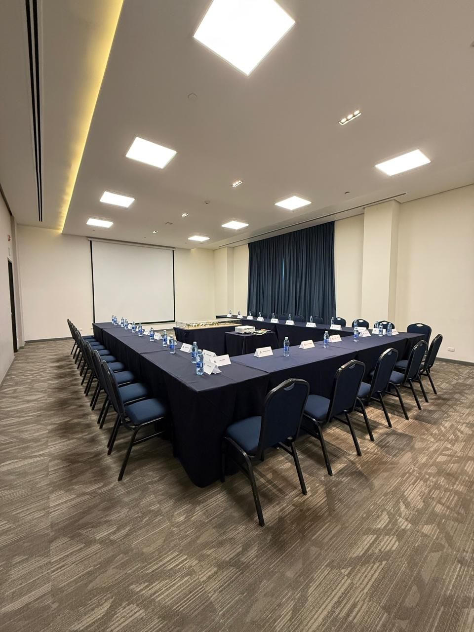 Una sala de conferencias con una mesa larga, sillas, tarjetas de identificación y una pantalla de proyector.