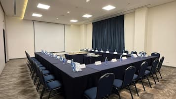 A conference room with a long table, chairs, nameplates, and a projector screen.