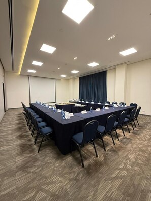 A conference room with a long table, chairs, nameplates, and a projector screen.