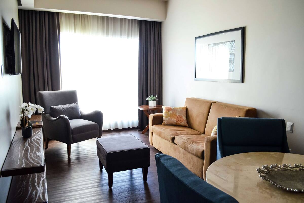 A modern living room with a sofa, armchair, ottoman, and a small round table.