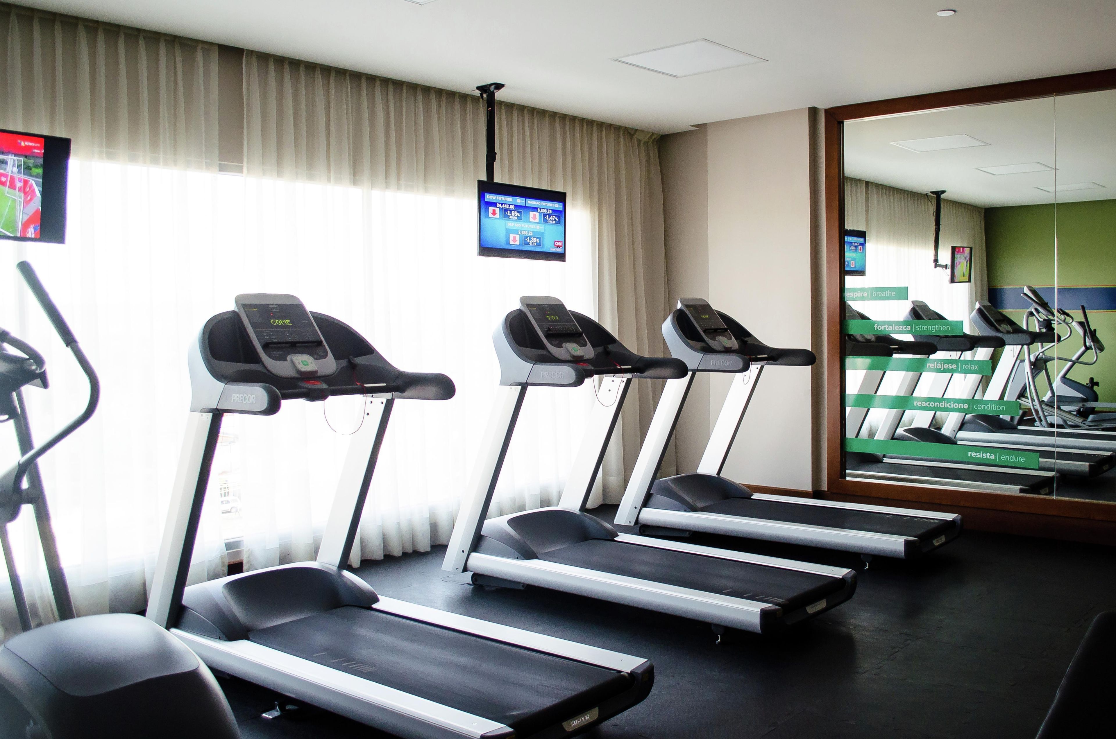 A fitness room with treadmills, a mirror, and a TV displaying financial news.
