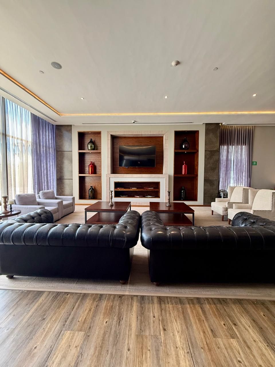 A modern living room with a fireplace, leather sofas, a flat-screen TV, and wooden shelves.