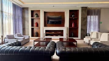 A modern living room with a fireplace, leather sofas, a flat-screen TV, and wooden shelves.