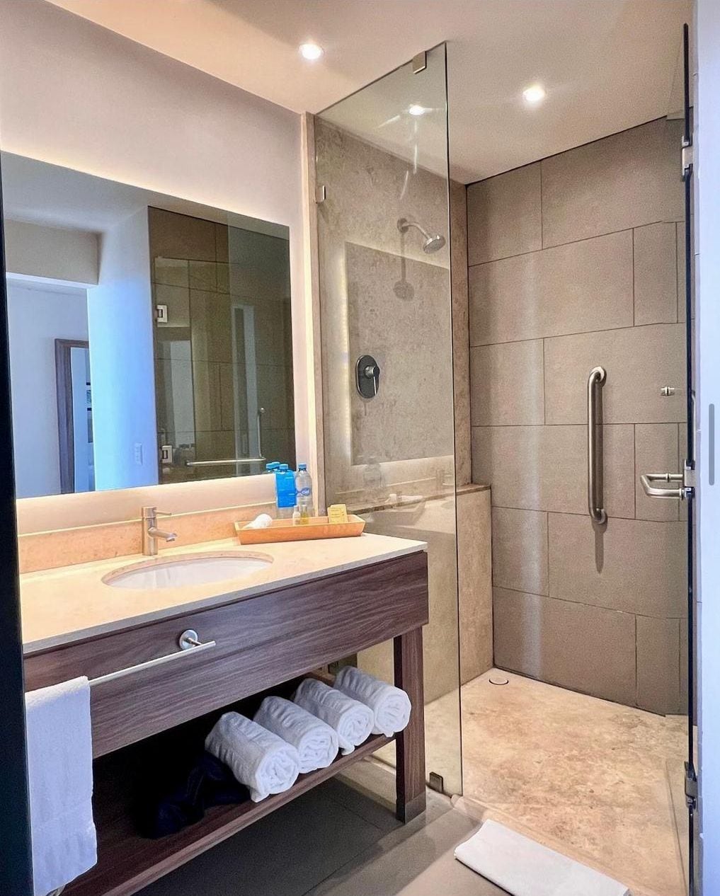 Un baño moderno con ducha envuelta en vidrio, tocador con espejo y perchero para toallas.