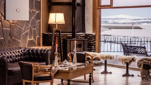 Un salon chaleureux avec un mur en pierre, une cheminée, un canapé en cuir, une table basse en bois et une vue sur l’eau.