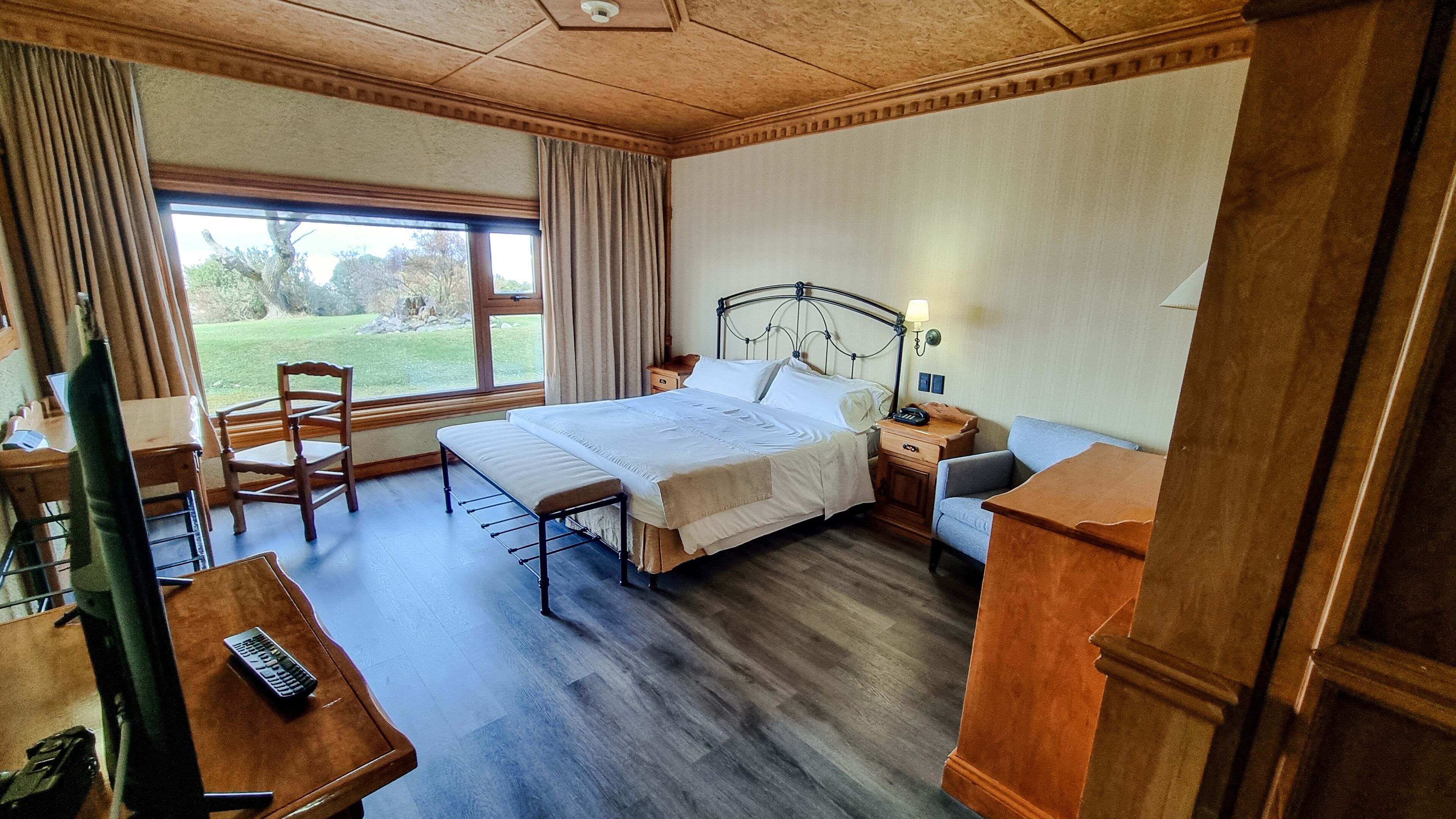 Habitación de hotel con cama, mesita de noche, silla, escritorio y vistas al exterior.