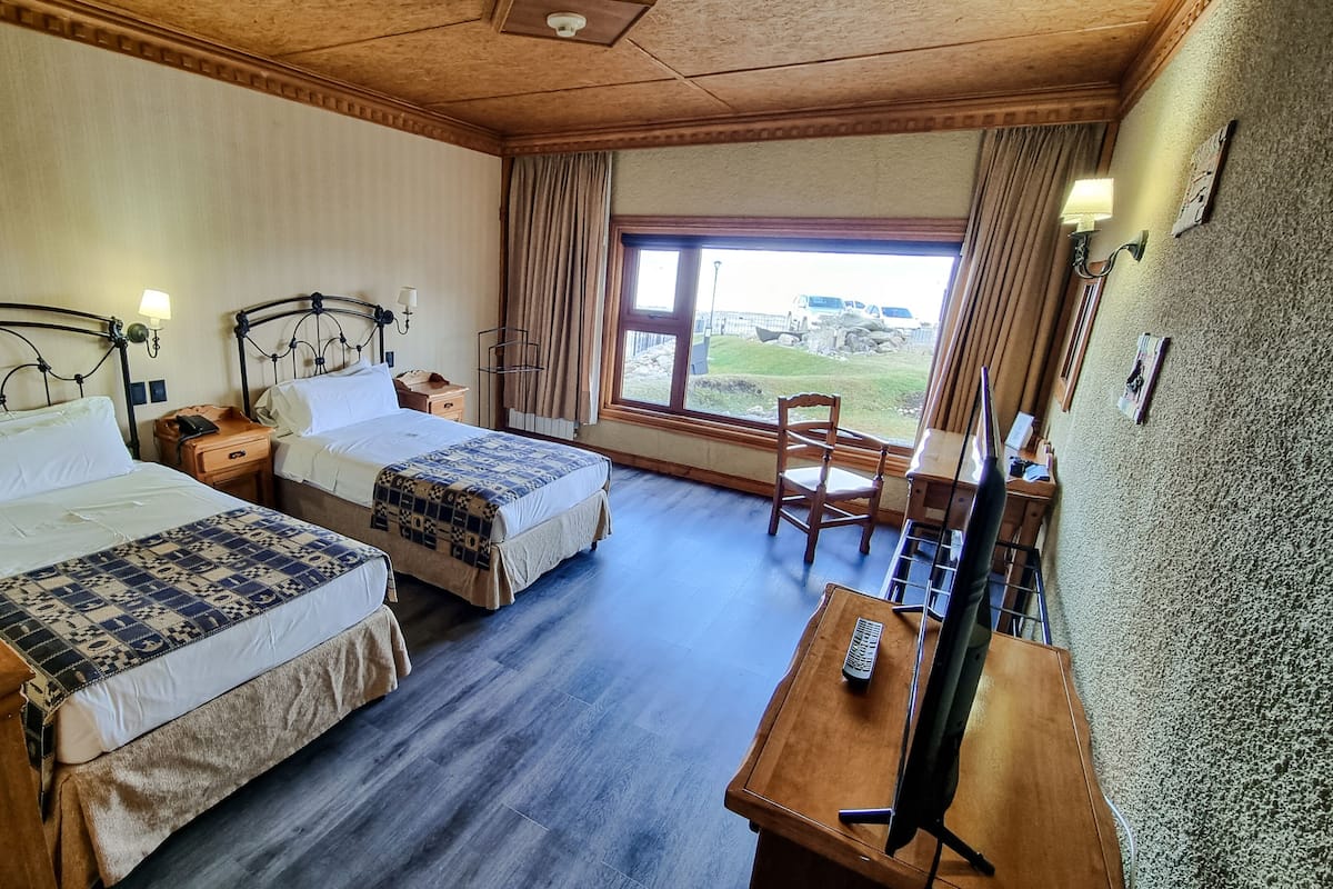A hotel room with two beds, a desk, a chair, and a window with a view.