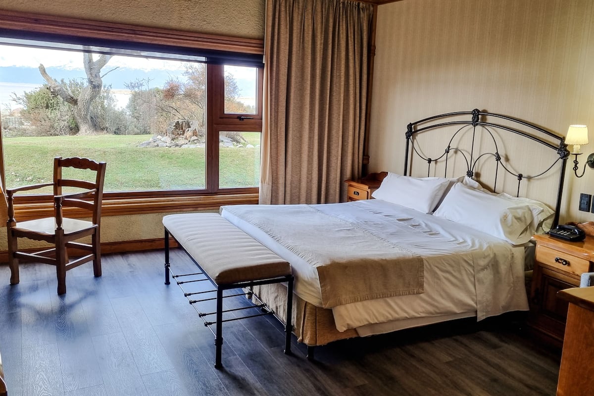 A hotel room with a bed, bedside tables, a chair, a lamp, and a view of the outdoors.