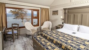 Une chambre d’hôtel avec un grand lit, deux fauteuils, une petite table et une fenêtre donnant sur la mer.