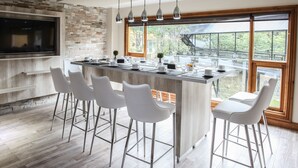 Une cuisine moderne dotée d’un îlot central, de tabourets de bar, d’une grande fenêtre et d’un téléviseur à écran plat fixé au mur.