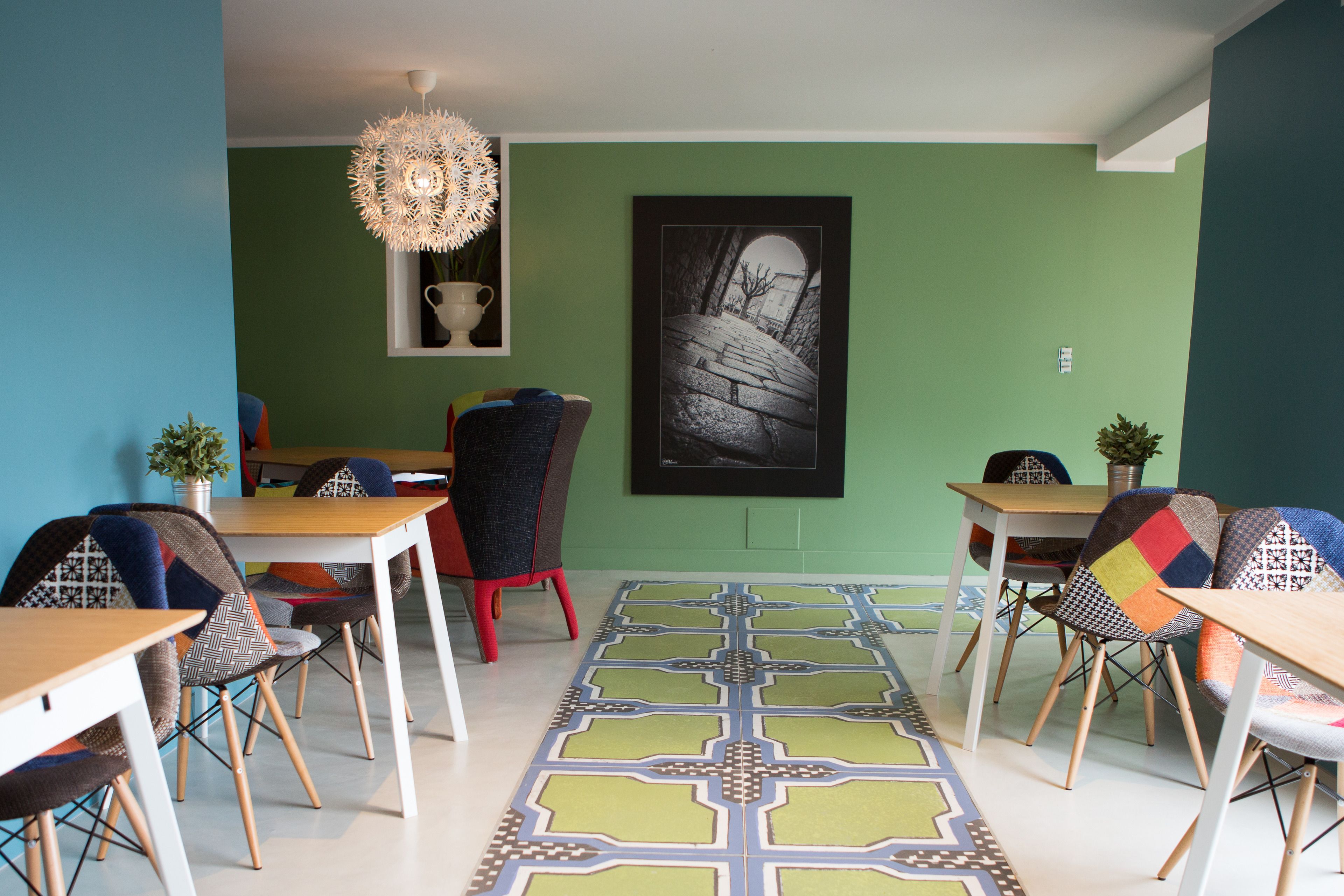 Een eethoek met een groene wand, een lijstwerkfoto en een patroonrijk vloerkleed.