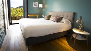 Un dormitorio con una cama grande, una mesita de noche con lámpara, y vistas a un balcón con plantas.