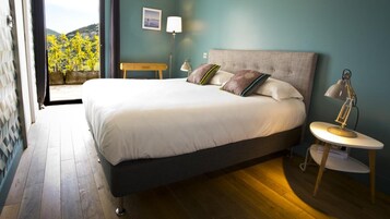 Quarto com uma cama grande, mesa de cabeceira com abajur, criadeira e vista para uma varanda com plantas.