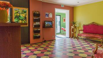 Un vestíbulo de hotel con mostrador de recepción, un escritorio de atención al cliente, un sofá rojo y un piso con baldosas de colores.
