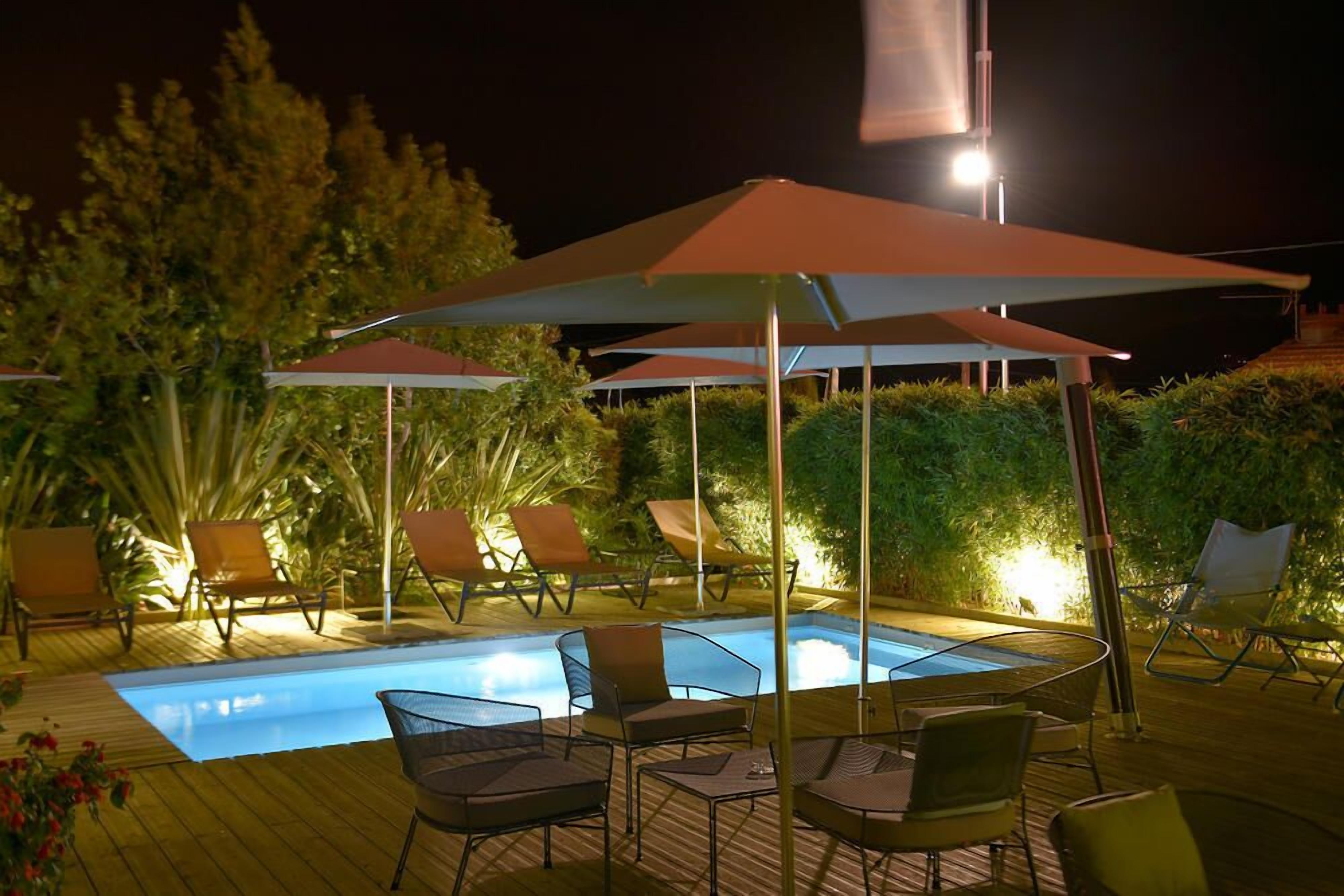 A pool area with lounge chairs and umbrellas, surrounded by greenery.