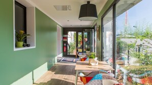 Una habitación moderna con un gran ventanal corredero que da a un balcón, piso de madera y una mesa con cojines y una planta en maceta.