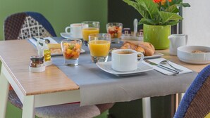 Una mesa de desayuno con una taza de café, un vaso de jugo de naranja, croissants y un frutero.