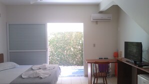 A hotel room with a bed, a desk with a computer, an air conditioner, and a view of greenery outside. - Floripa Lodge Pousada & Bistrô (Florianópolis)