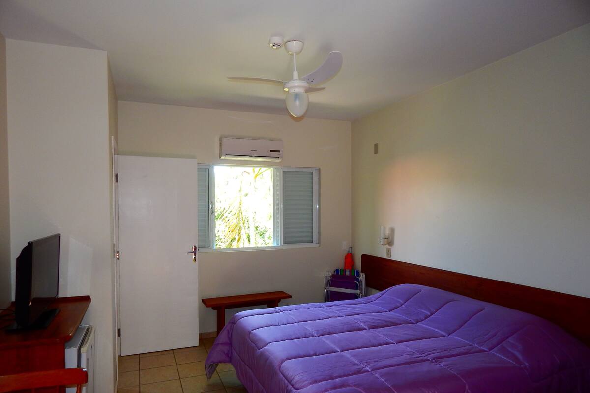 A room with a bed, a desk, a chair, a television, a window, and a ceiling fan.