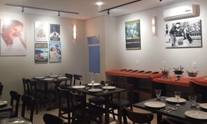 A restaurant with multiple tables set for dining, featuring posters on the walls and an air conditioning unit above. - Floripa Lodge Pousada & Bistrô (Florianópolis)