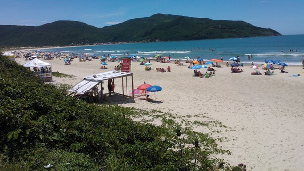 A beach with umbrellas, tents, and people. - Floripa Lodge Pousada & Bistrô (Florianópolis)