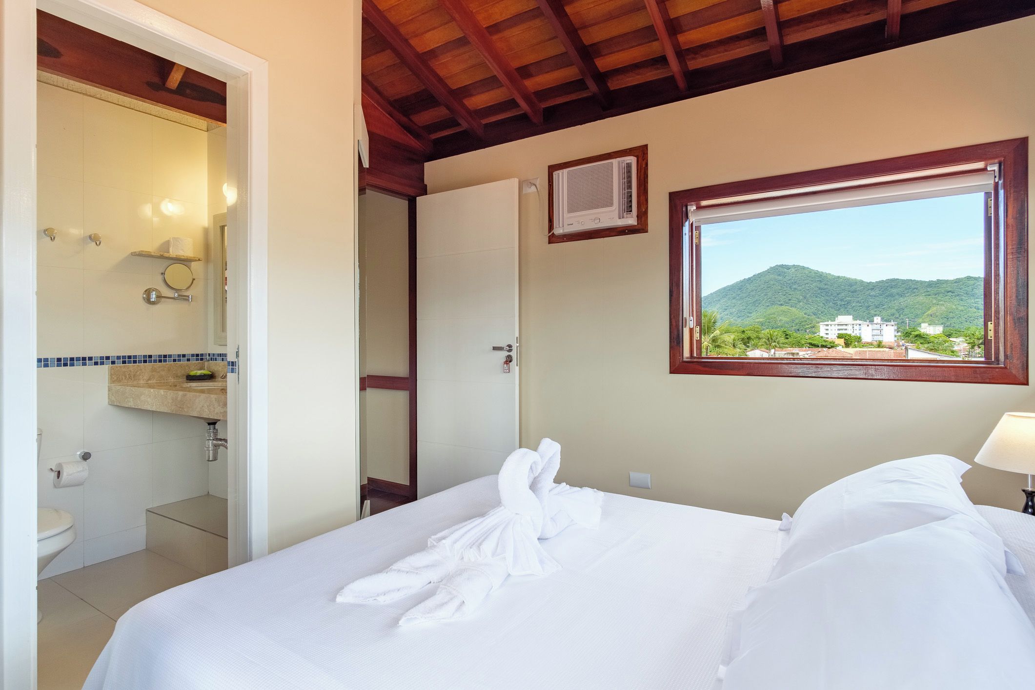 A hotel room with a bed, a bathroom, and a window with a view of a mountain.