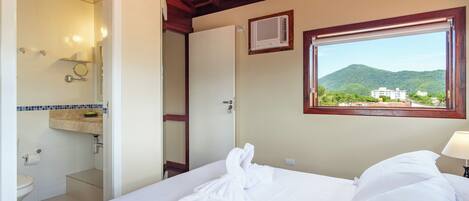 A hotel room with a bed, a bathroom, and a window with a view of a mountain.