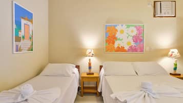 Una habitación de hotel con dos camas, ropa de cama blanca, una mesita de noche de madera con una lámpara y un cuadro de flores en la pared.