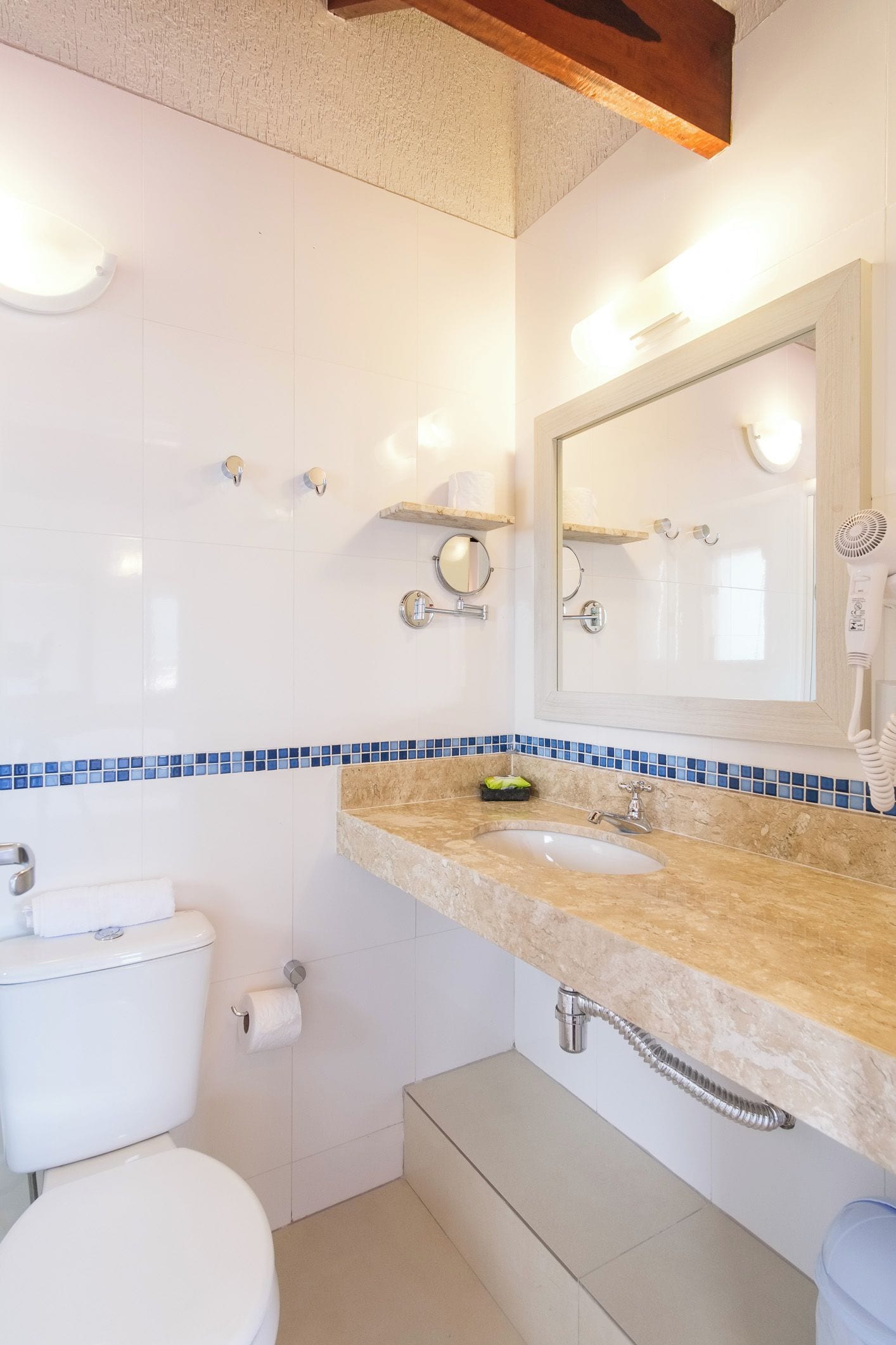 Un baño con inodoro, lavamanos, espejo y toallero.