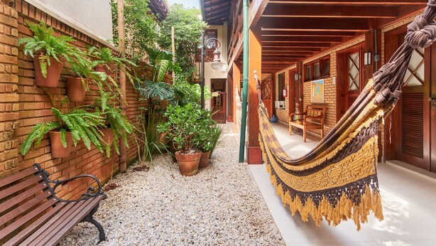 A courtyard with a hammock, potted plants, a bench, and a brick wall. - Pousada Don Diego (Ubatuba)