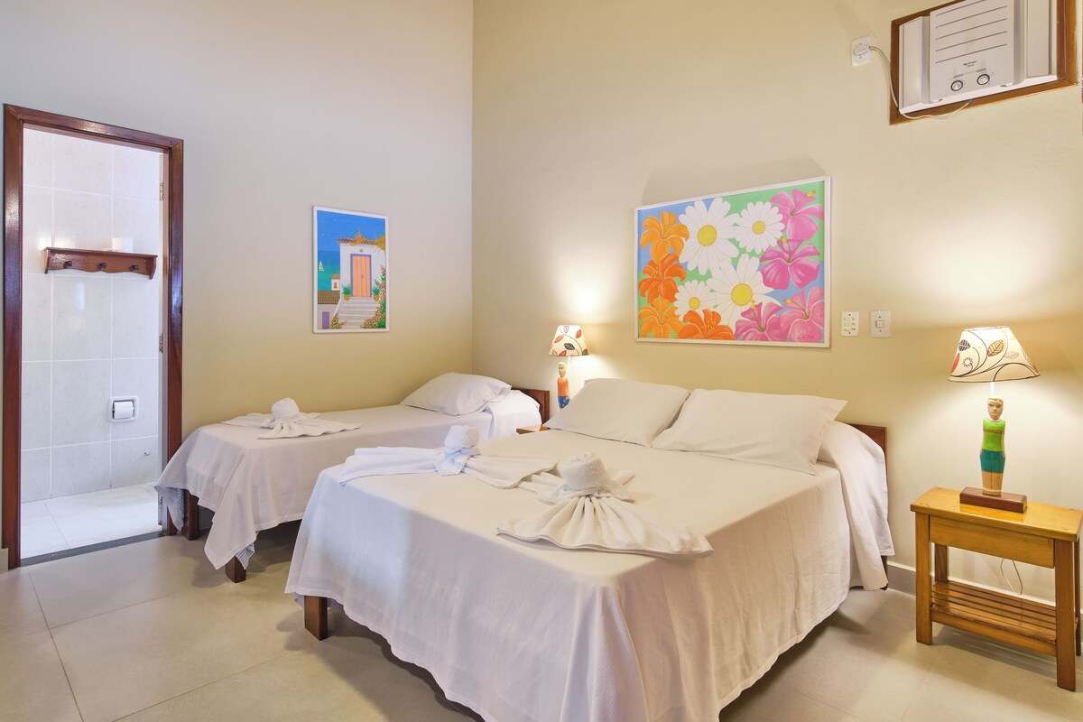 A hotel room with two beds, a wooden nightstand, a wall-mounted air conditioner, and a door leading to a bathroom.