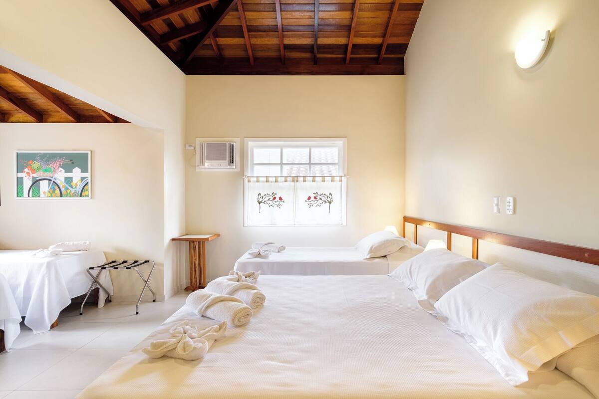 Habitación de hotel con dos camas, una ventana con cortinas decorativas, un cuadro en la pared y un techo con vigas a la vista.