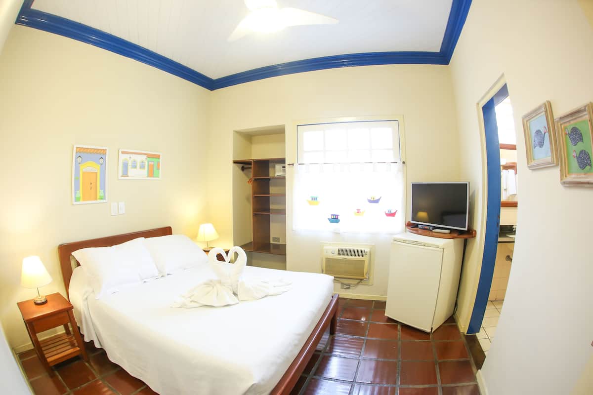 Habitación de hotel con cama, lámparas de noche, televisor, refrigerador pequeño y ventana con vista a barcos.