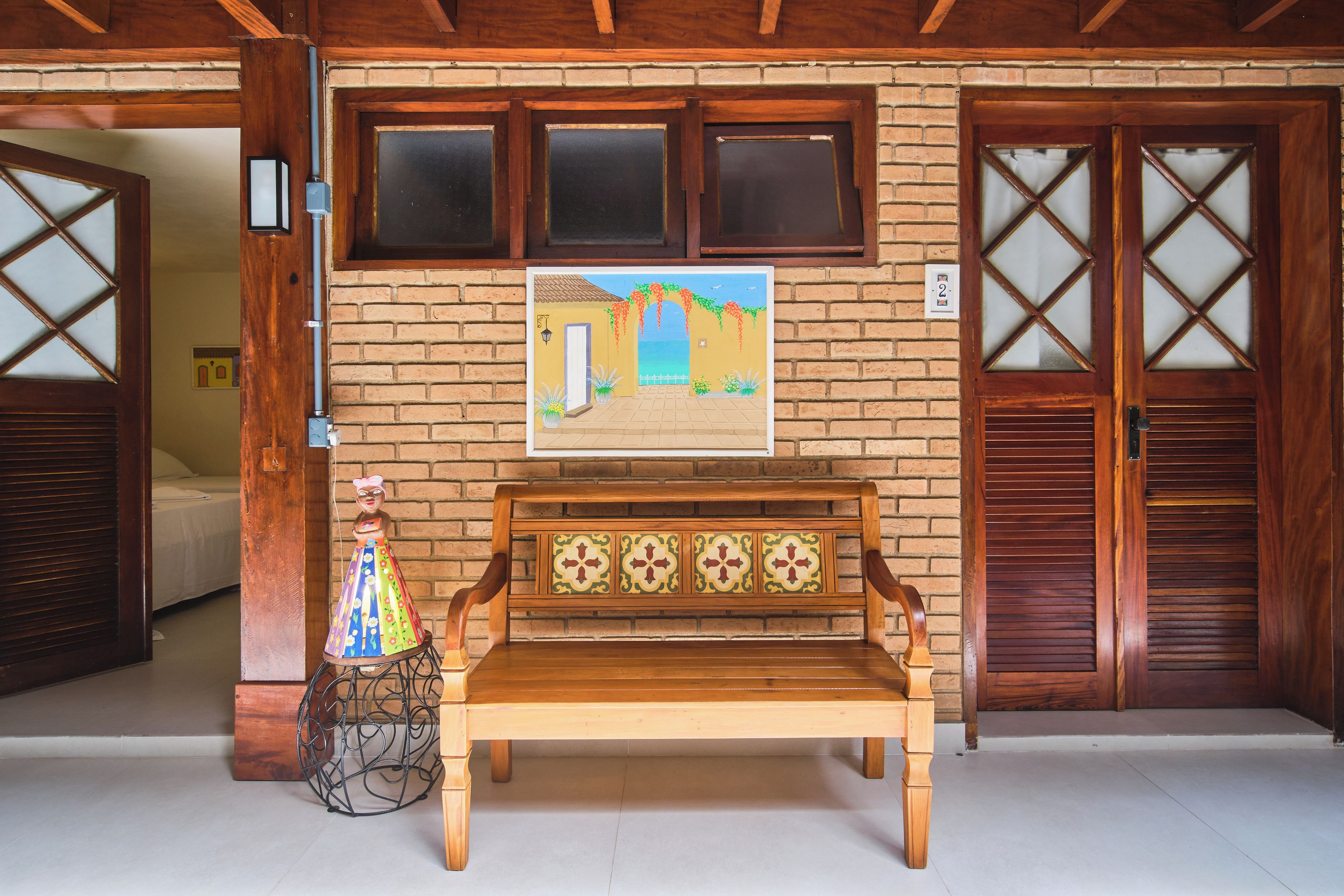 Um banco de madeira sobre piso de azulejos, uma parede com um mural pintado e uma porta com janela.