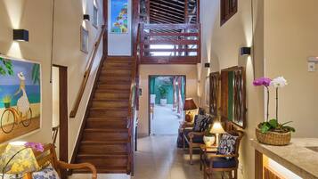 A spacious hallway with a wooden staircase, wicker pendant lights, and a reception desk with a plant.
