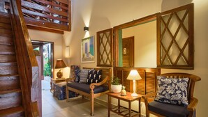A cozy living room with a wooden staircase, a sofa with cushions, a small table with a lamp, and a chair with a patterned cushion. - Pousada Don Diego (Ubatuba)