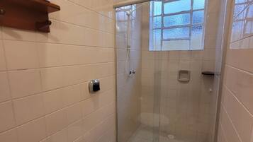 Een badkamer met toilet, een glazen douchecabine, een handdoekrek en een raam.