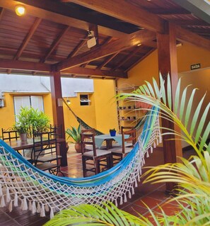Relax in a patio area with a hammock, wooden chairs, and a table, surrounded by lush greenery.