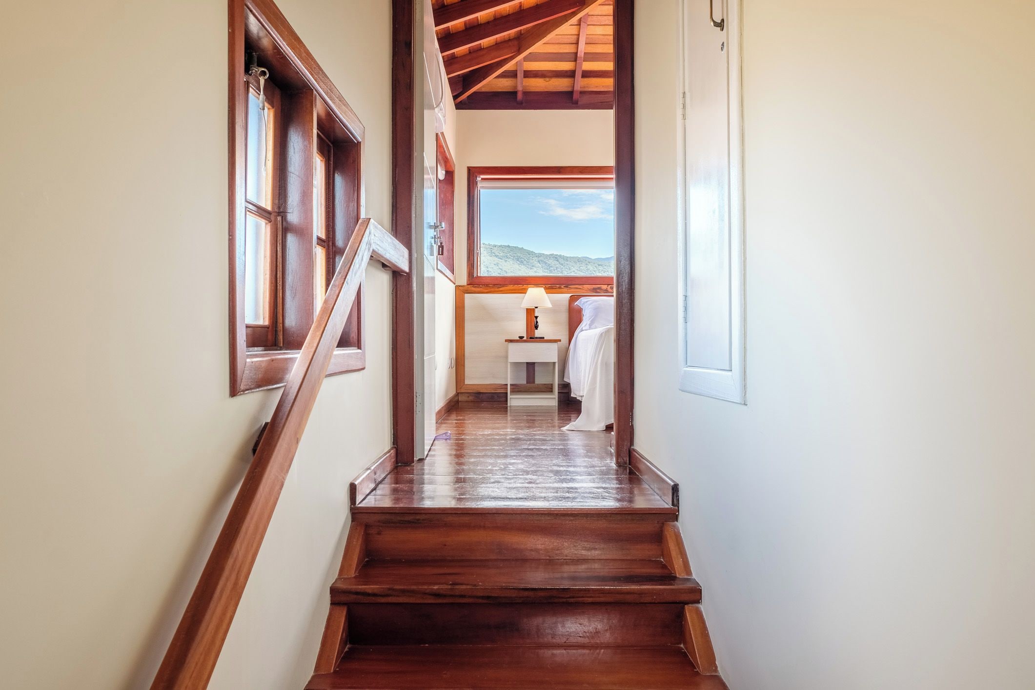 A wooden staircase leading to a room with a bed and a window overlooking a landscape.