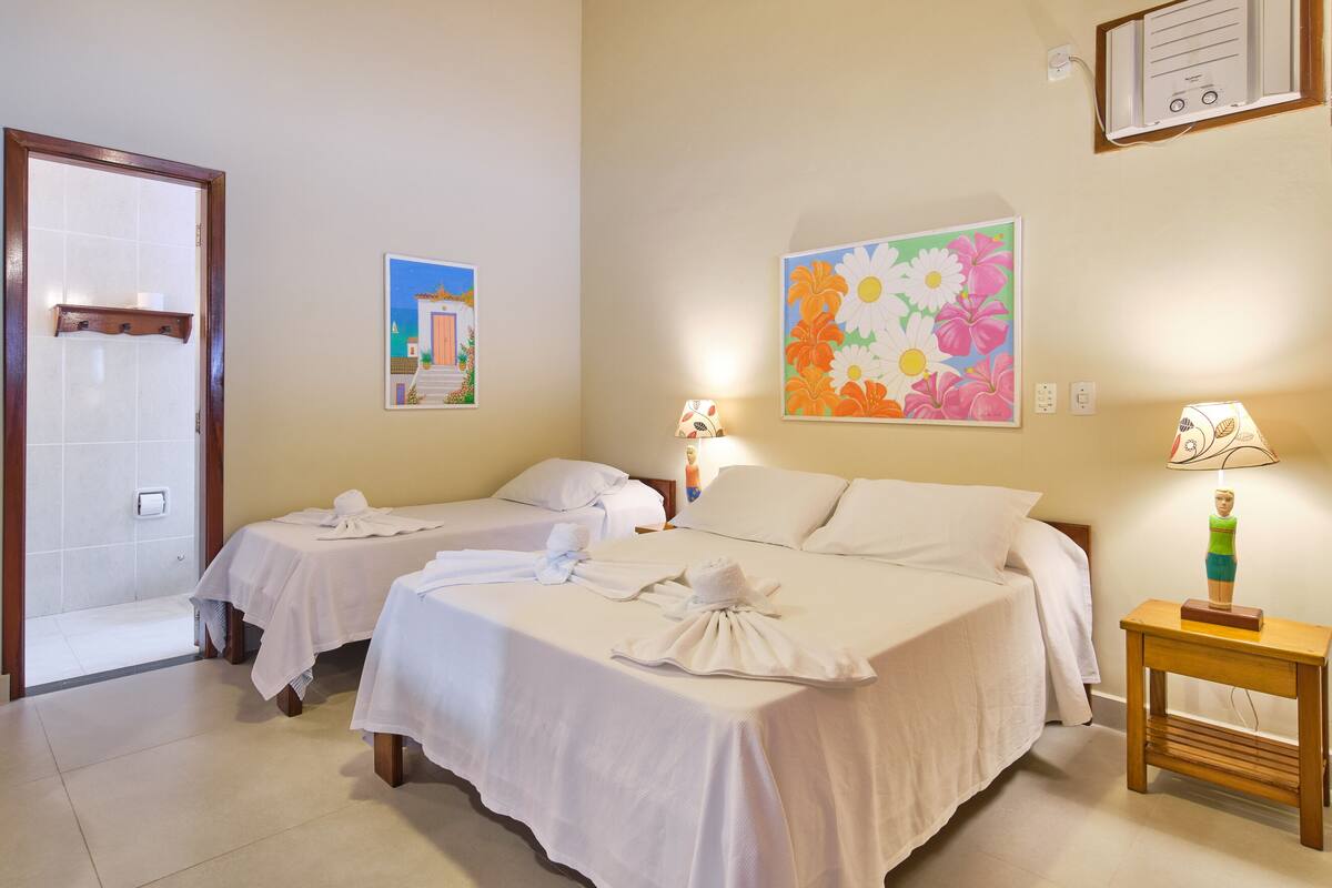 Habitación de hotel con dos camas, una mesita de noche de madera, aire acondicionado montado en la pared y una puerta que da al baño.