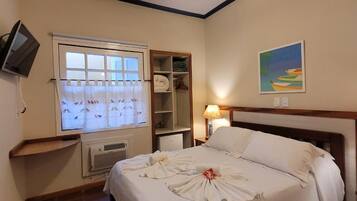 Une chambre d’hôtel avec un lit, un ventilateur de plafond, une fenêtre avec des rideaux, un tableau au mur et un téléviseur fixé au mur.