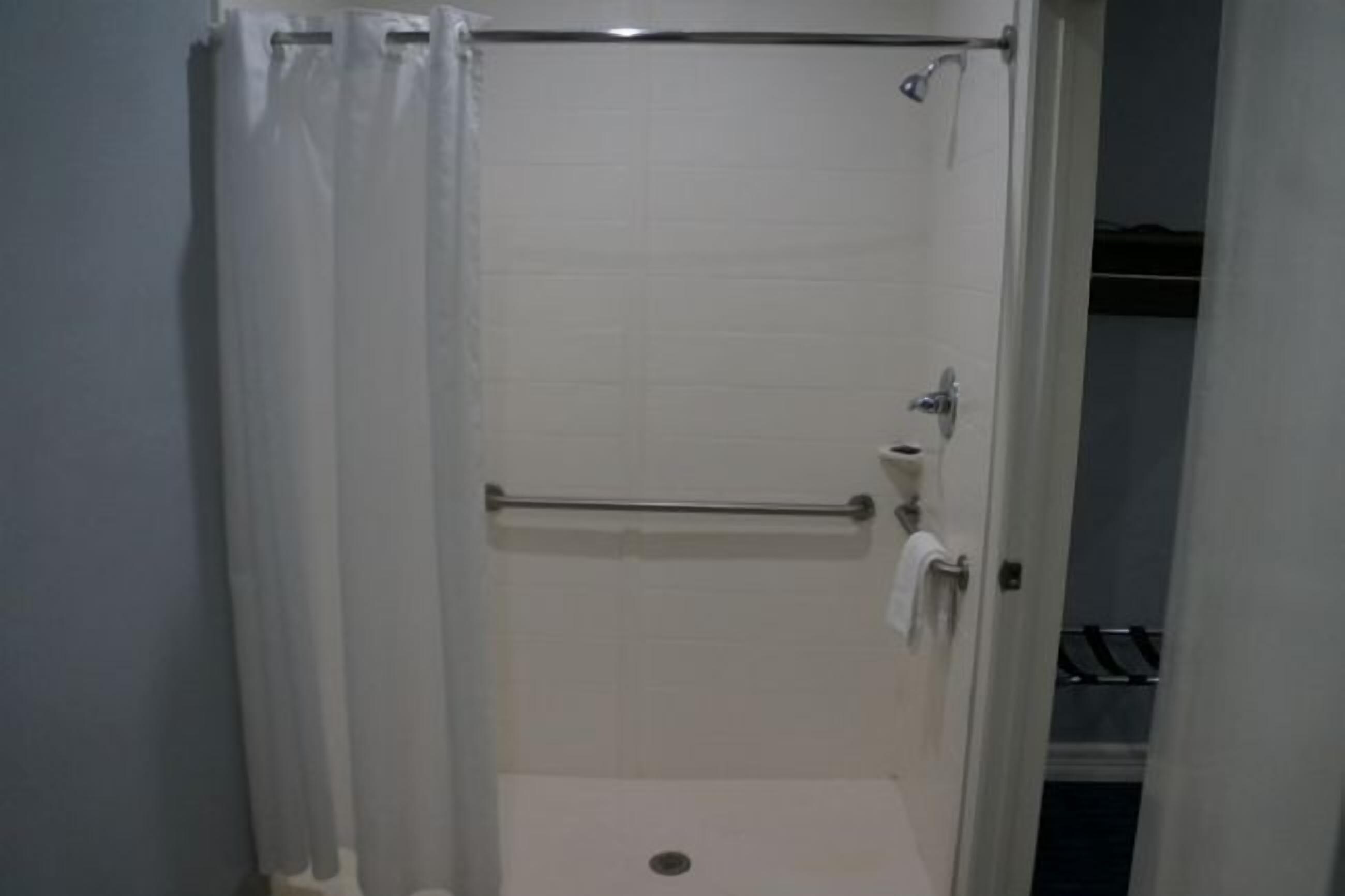 A small, enclosed shower area with a metal grab bar, a towel rack, and a door leading to a closet.