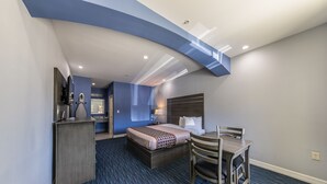 A hotel room with a bed, desk, chair, and a small kitchenette area. - Home Place Inn Spring I-45 North & 1960 (Houston)