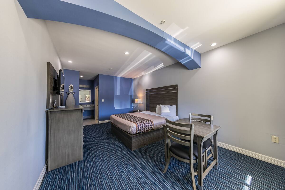 A hotel room with a bed, desk, chair, and a small kitchenette area.