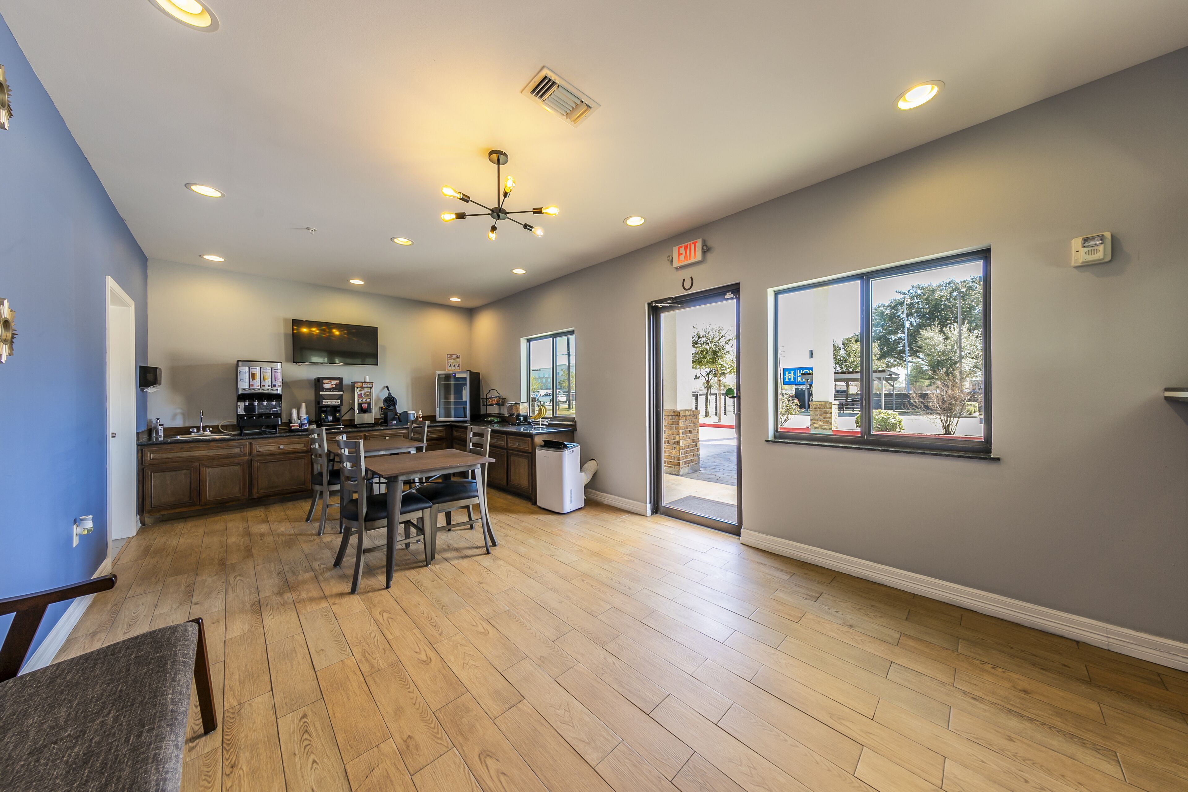 A modern kitchen with wooden cabinets, a dining area with a table and chairs, and large windows offering a view of the outside.