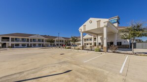 A hotel with a covered parking area, multiple buildings, and a clear blue sky. - Home Place Inn Spring I-45 North & 1960 (Houston)