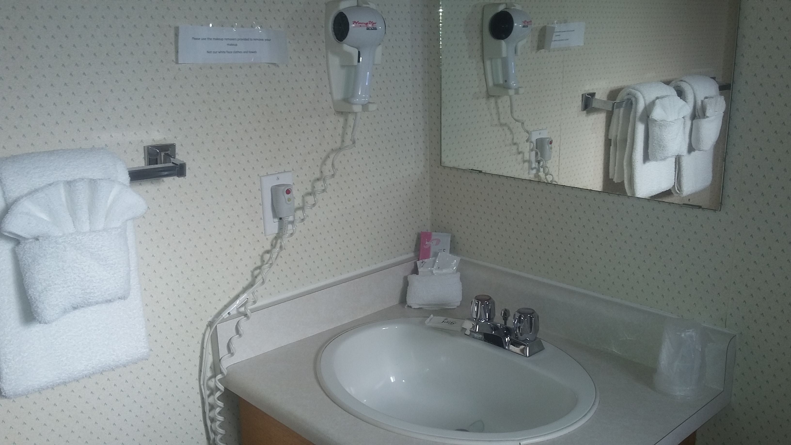 Een badkamer met een wit wastafel, twee haardroger, een handdoekhouder en een spiegel.