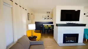 Una sala de estar moderna con un sofá, un sillón amarillo, una chimenea y un televisor montado en la pared.