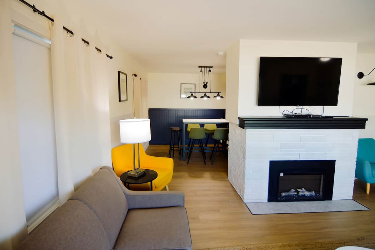 A modern living room with a sofa, a yellow chair, a fireplace, and a TV mounted on the wall.