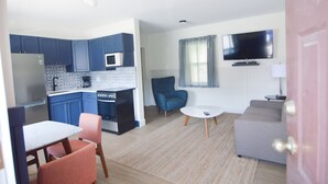 Un espacio habitable compacto con kitchenette, zona de comedor, sofá y televisor montado en la pared.